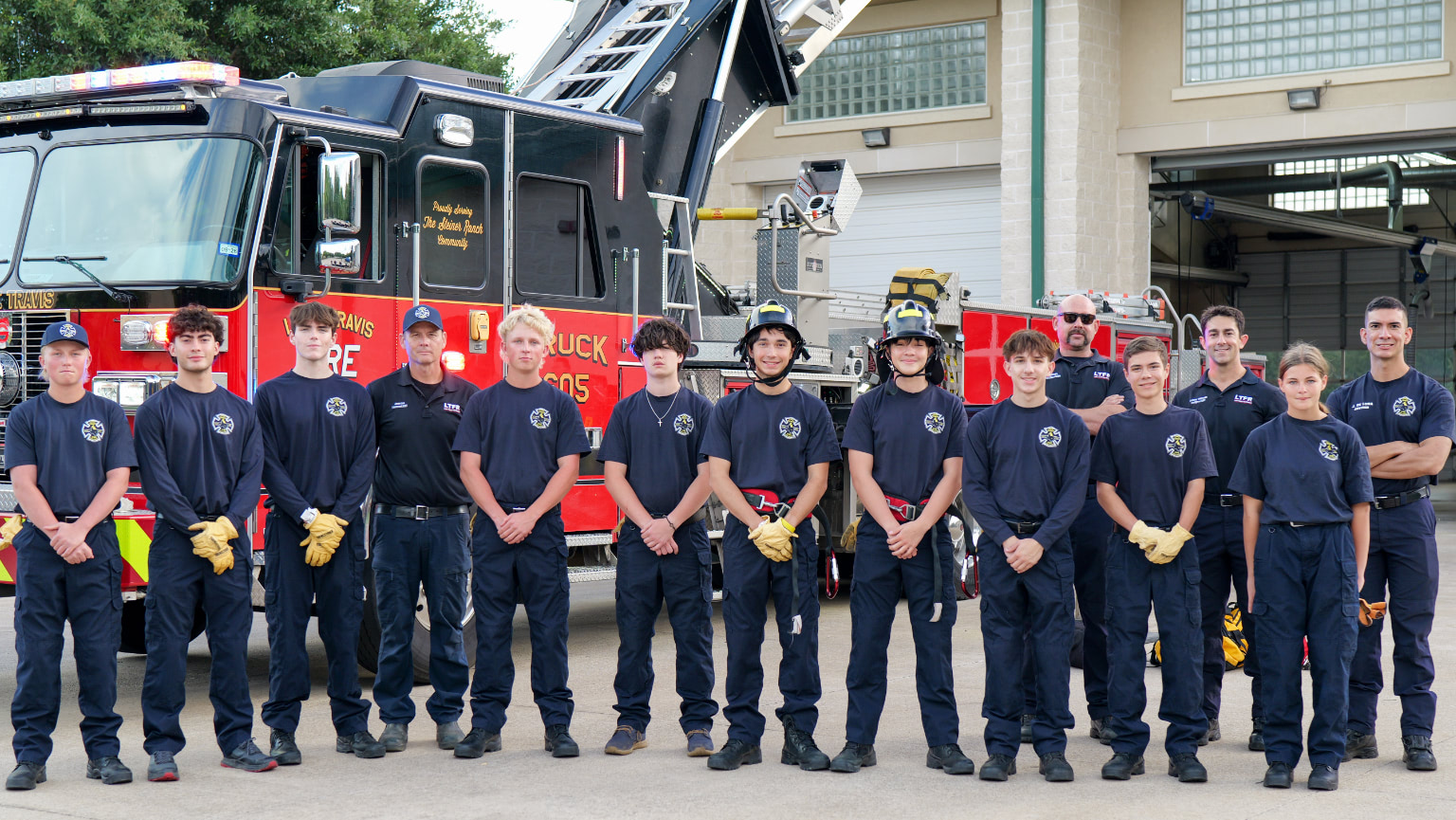 Group of firefighter Explorer trainees and instructors posing in front of a fire engine at the fire station.